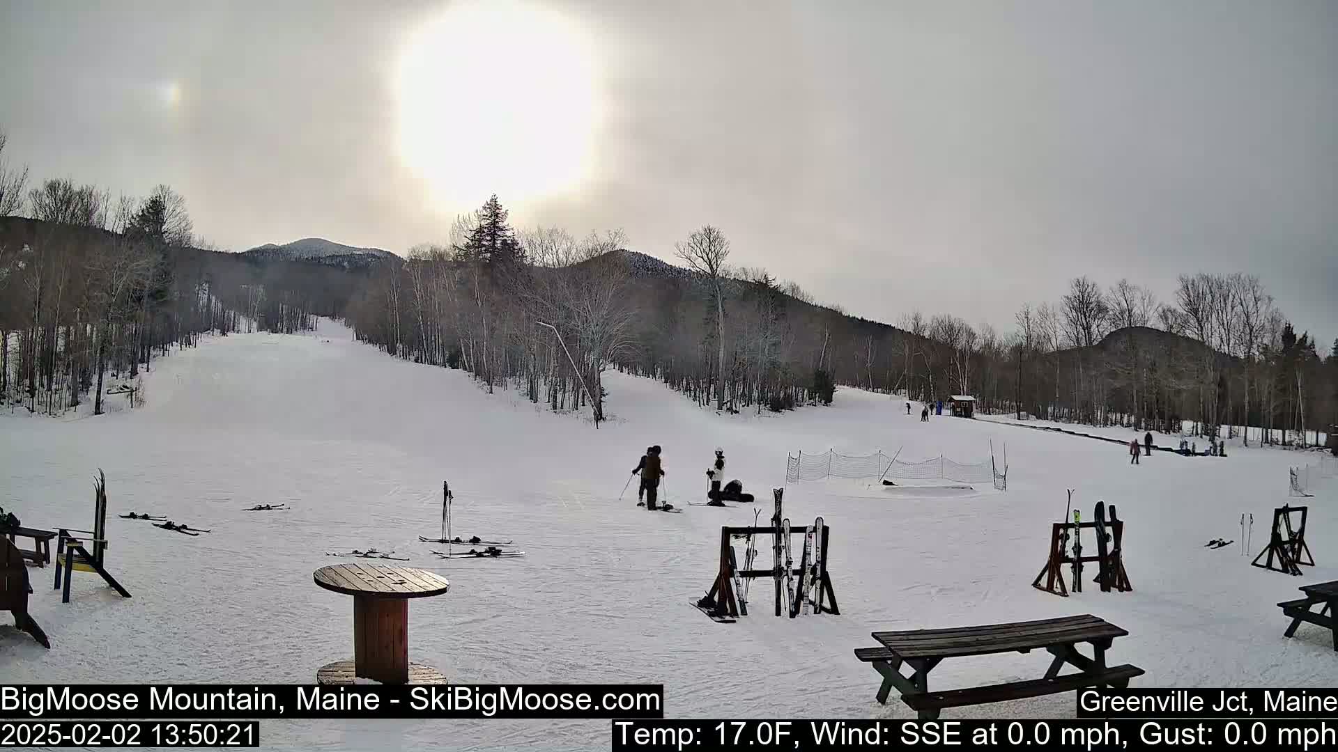 A mostly sunny, but overcast, snowy ski slope with a few people and ski equipment.