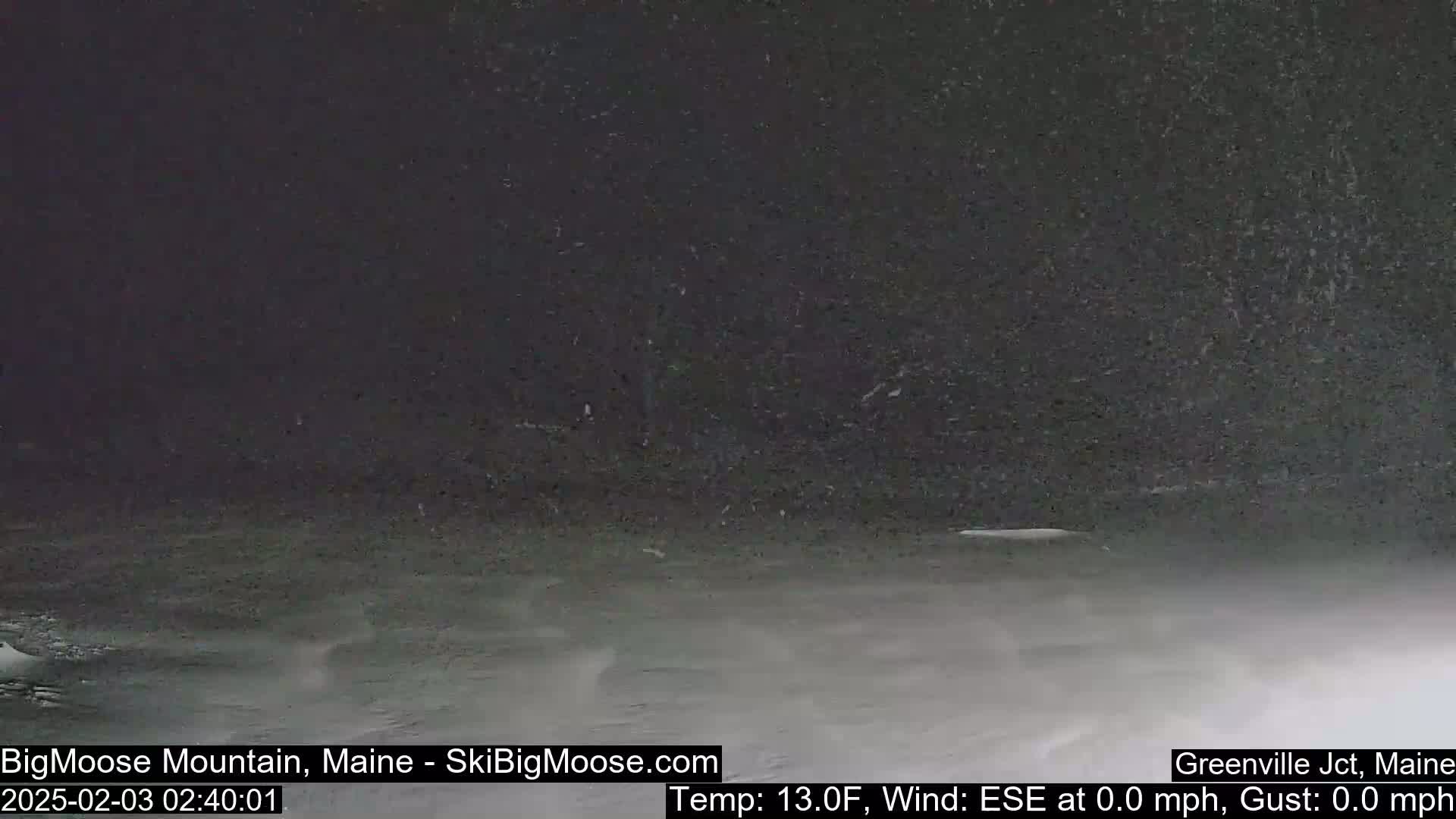 A snowy, dark scene shows a flat, snow-covered ground under a night sky with falling snow.