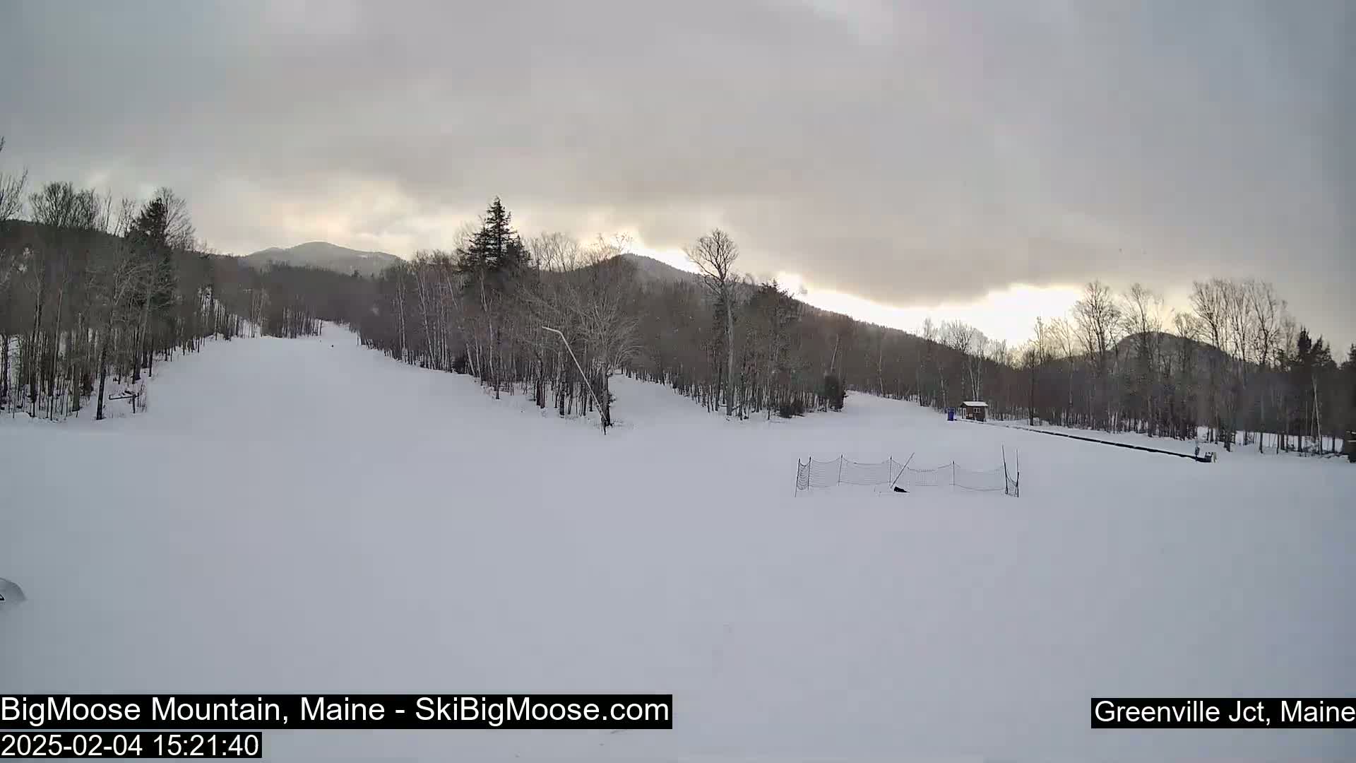 A snow-covered ski slope with bare trees and a cloudy sky is visible.