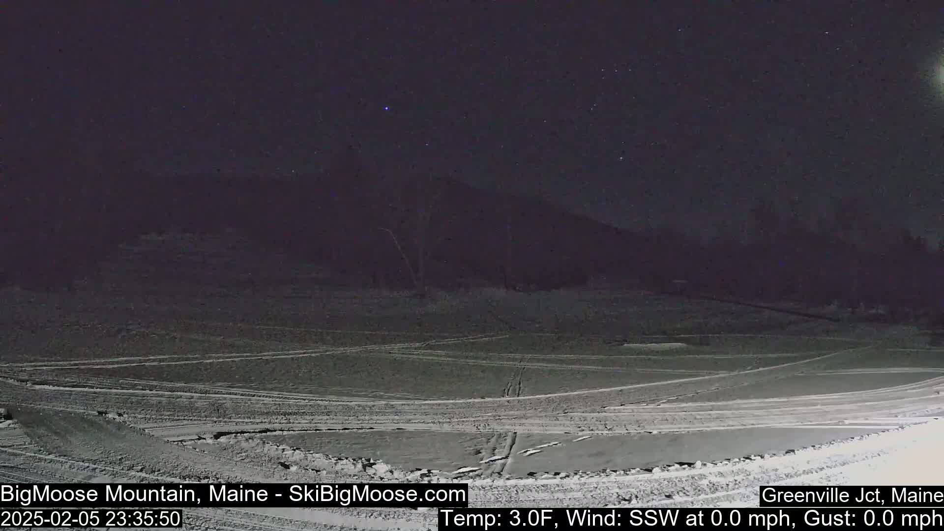 A snow-covered, flat area is visible at night under a starry sky, with a dark mountain in the background.