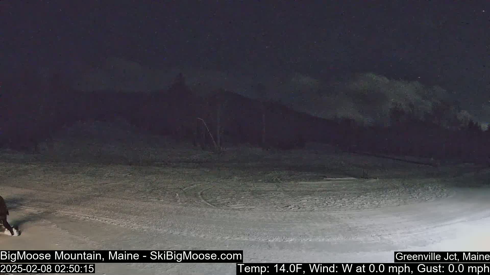A snow-covered area at night, with a dark mountain in the background under a clear, starry sky.