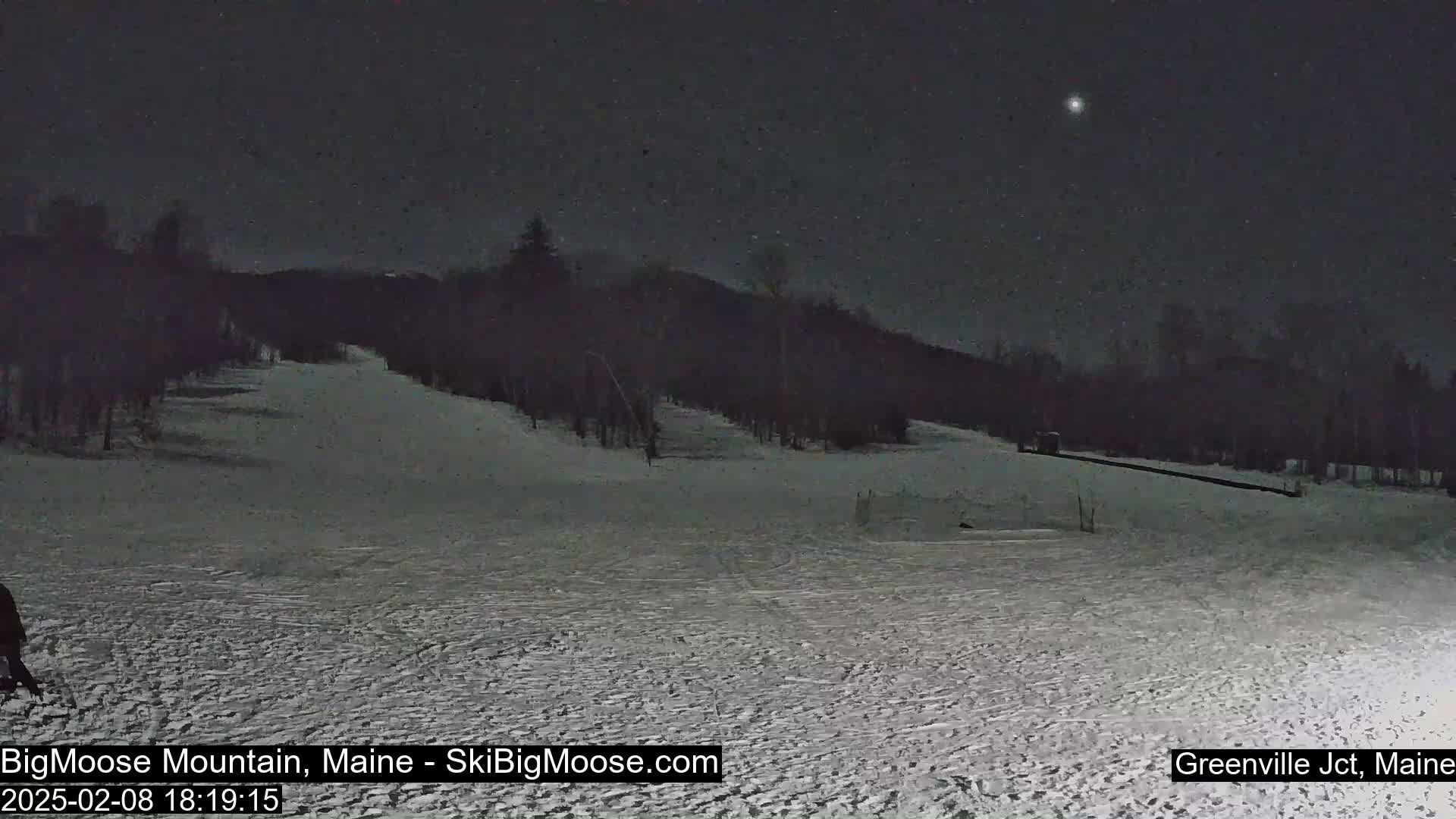 A snow-covered ski slope is visible at night under a lightly snow-filled sky with a bright star.