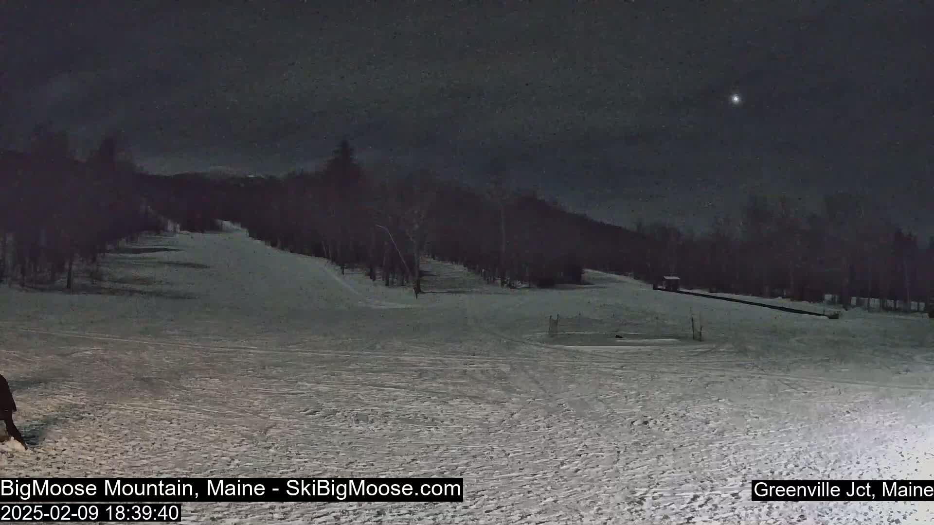 A snow-covered ski slope at night under a dark, clear sky with a single bright star visible.