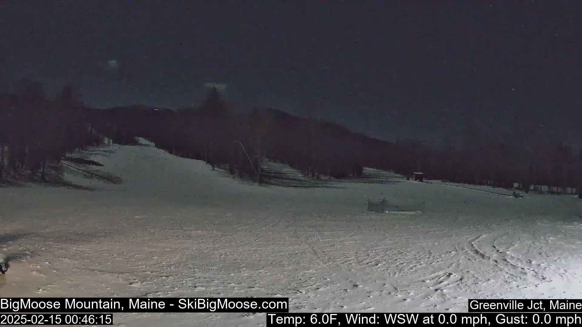 A snow-covered ski slope is visible at night under a dark sky, with calm weather conditions.