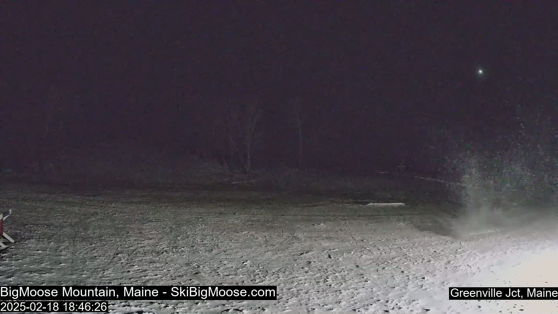 A snow-covered, dark landscape is visible at night, with light snow falling.