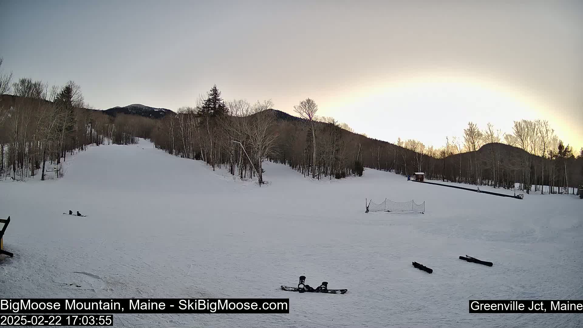 A snow-covered ski slope with a few pieces of snow sports equipment sits under a pale sunset sky.
