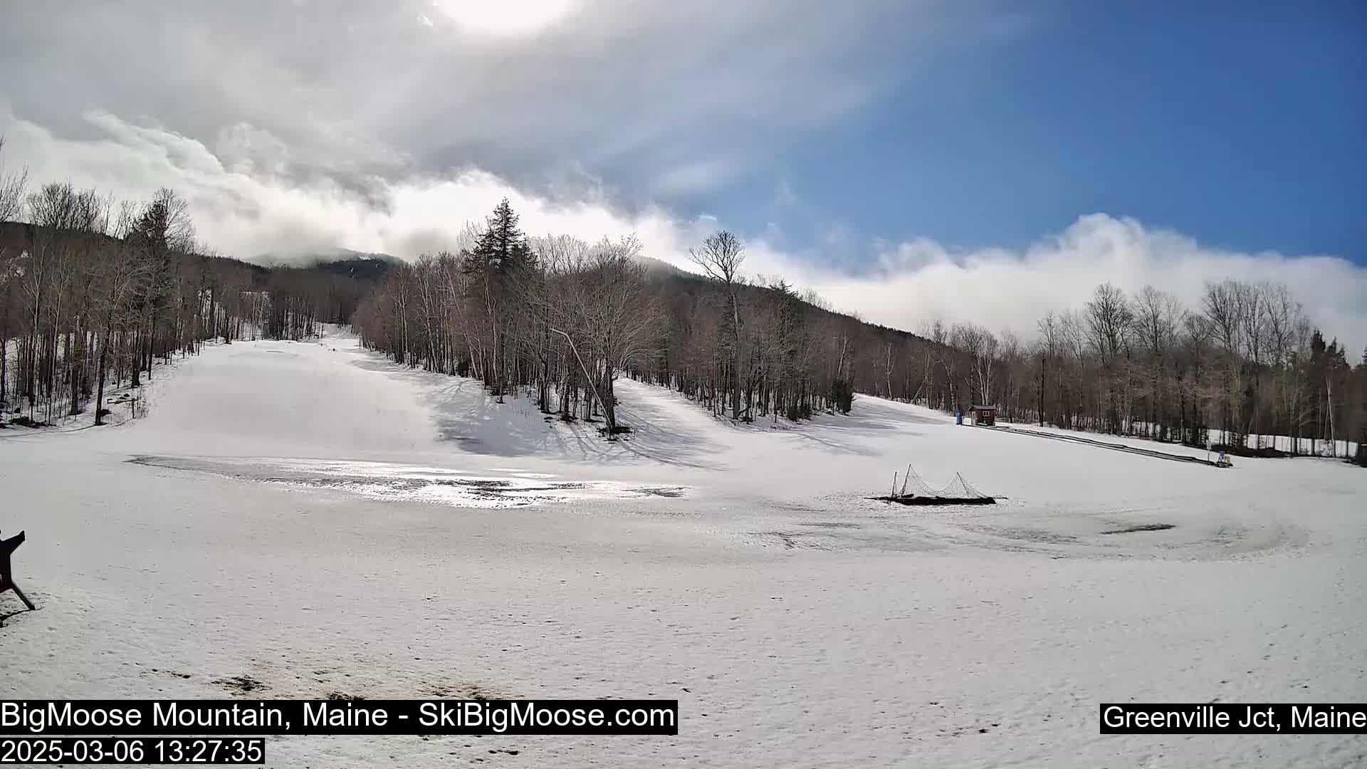 A snow-covered ski slope with bare trees and partly cloudy skies is visible.