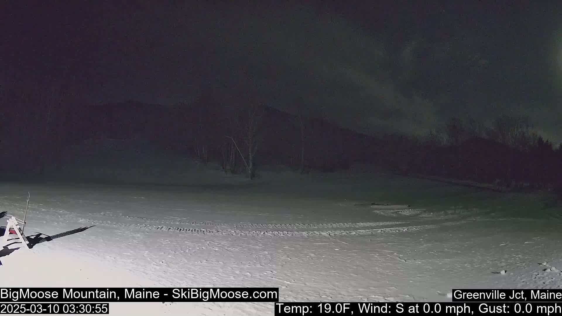 A snow-covered area at night, under a dark sky with some clouds, is illuminated by artificial light.