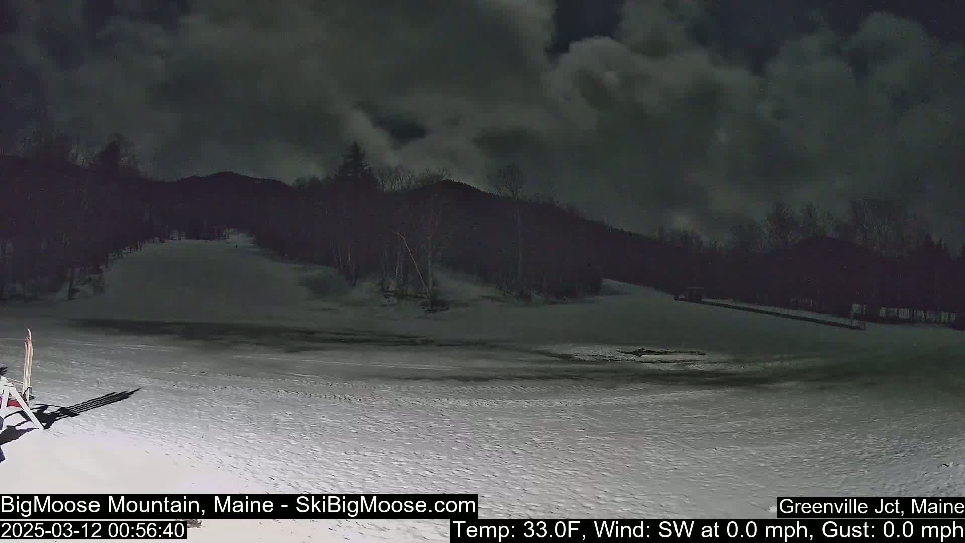 A snow-covered ski slope at night under a cloudy sky, with a calm, 33°F temperature.