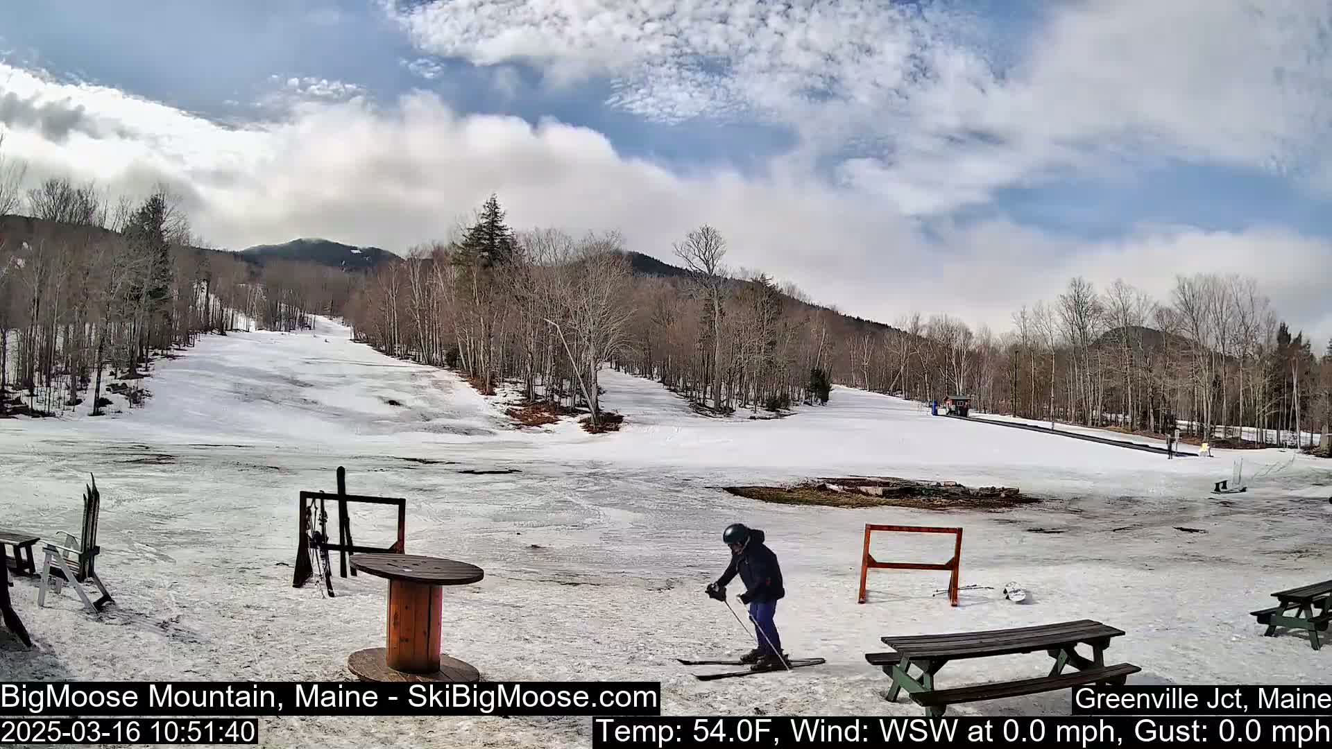A person skis on a snow-covered slope at a ski resort under a partly cloudy sky.
