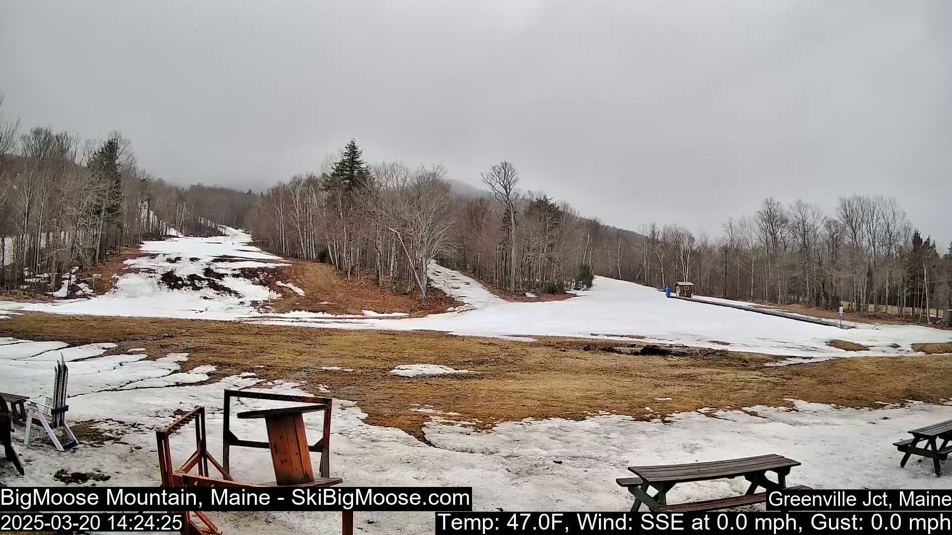 A mostly snow-covered ski slope with bare patches of brown ground is visible under an overcast sky.