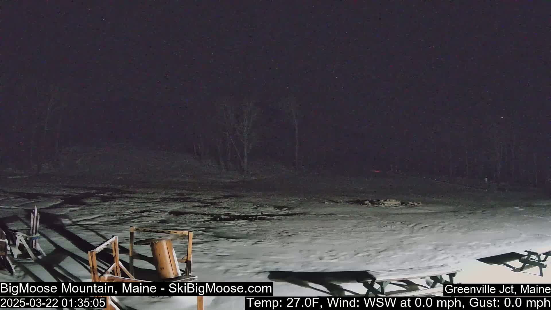 A snow-covered area at night with some picnic tables and other outdoor furniture, under a clear, starry sky.
