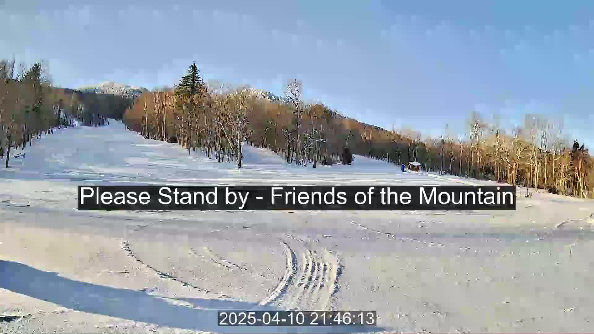 A snow-covered ski slope is visible, with leafless trees lining the hills in the background under a bright, sunny sky.