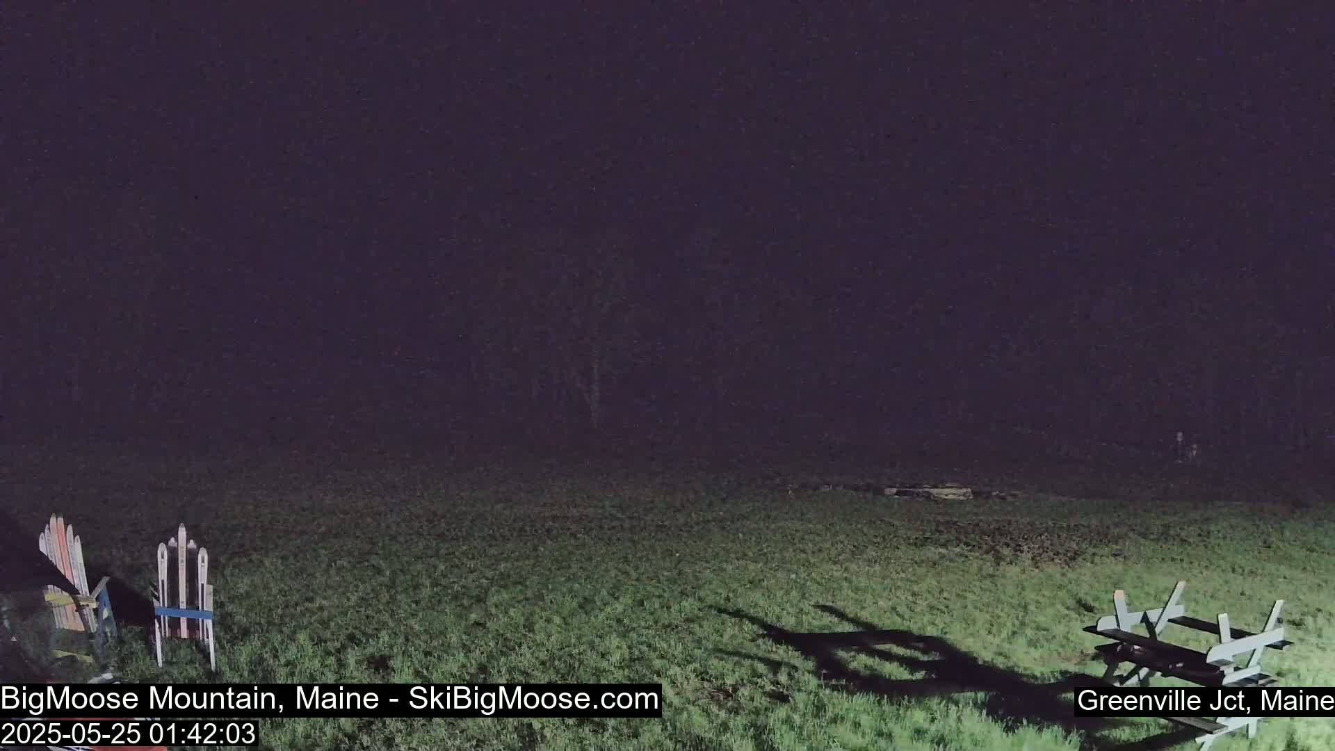 A nighttime view of a grassy field with a picnic table and skis in the foreground under a dark sky.