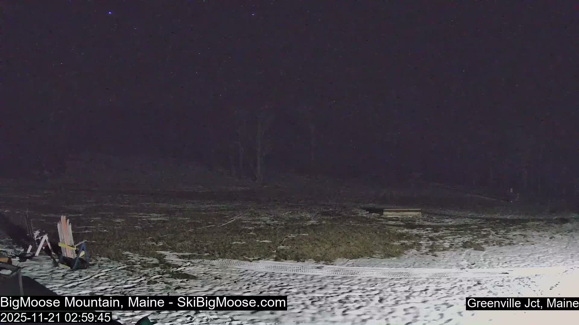 A clear night reveals a snowy, outdoor landscape with several chairs in the foreground and a dark forest in the background.
