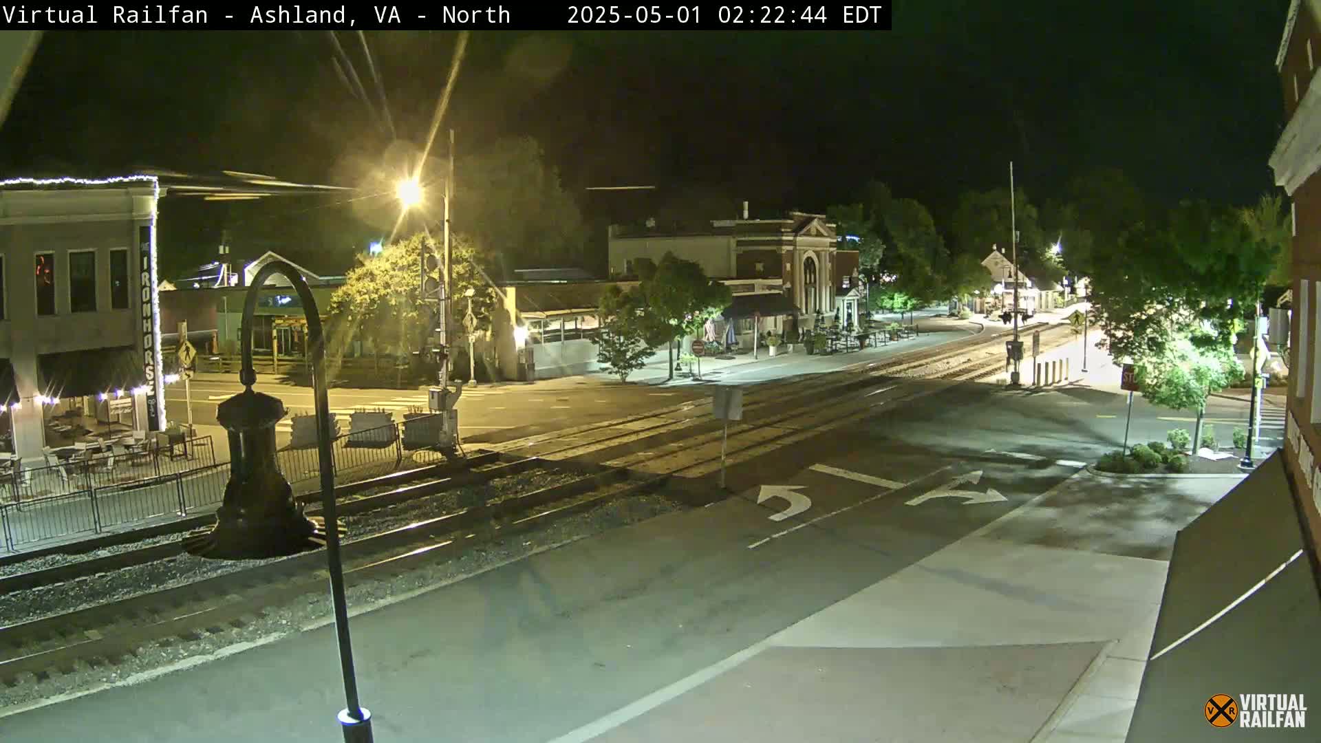 A nighttime view of a town square with train tracks running through it, under clear skies.