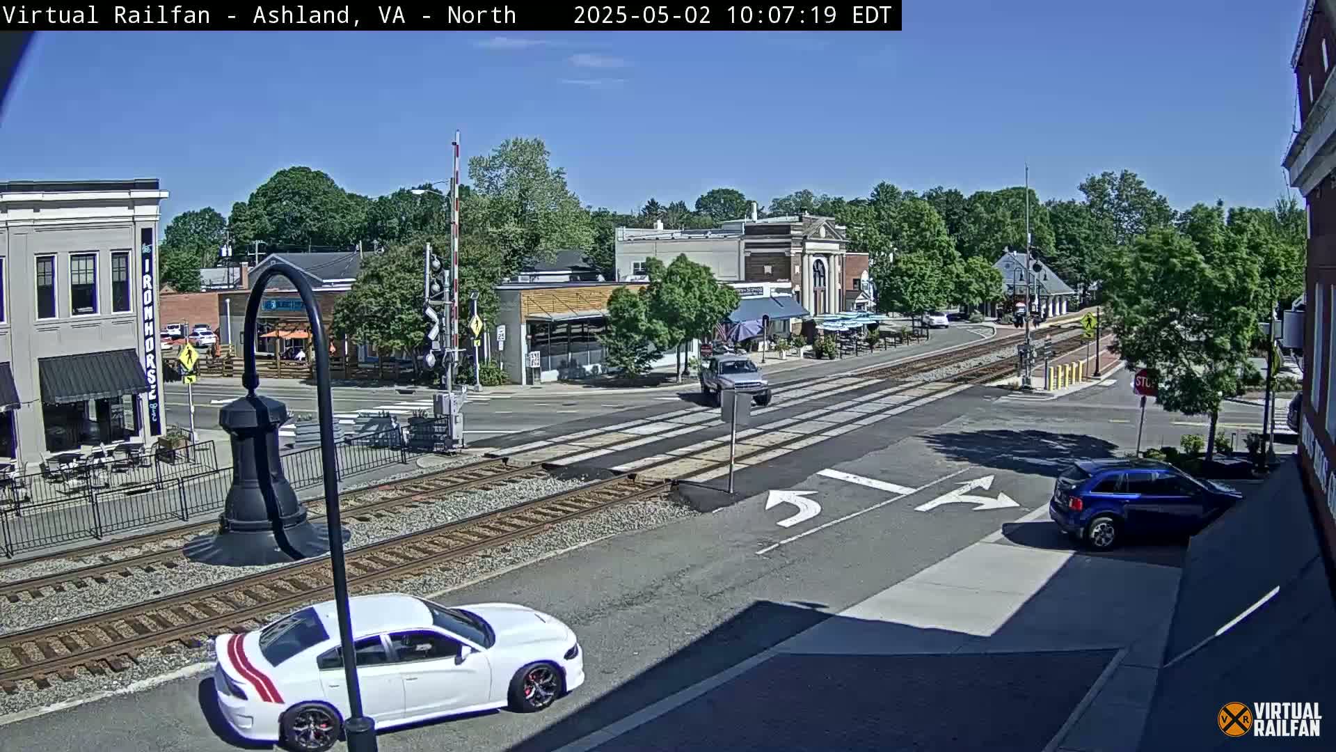 A sunny day view of a town intersection with railroad tracks, several cars, and buildings including restaurants.