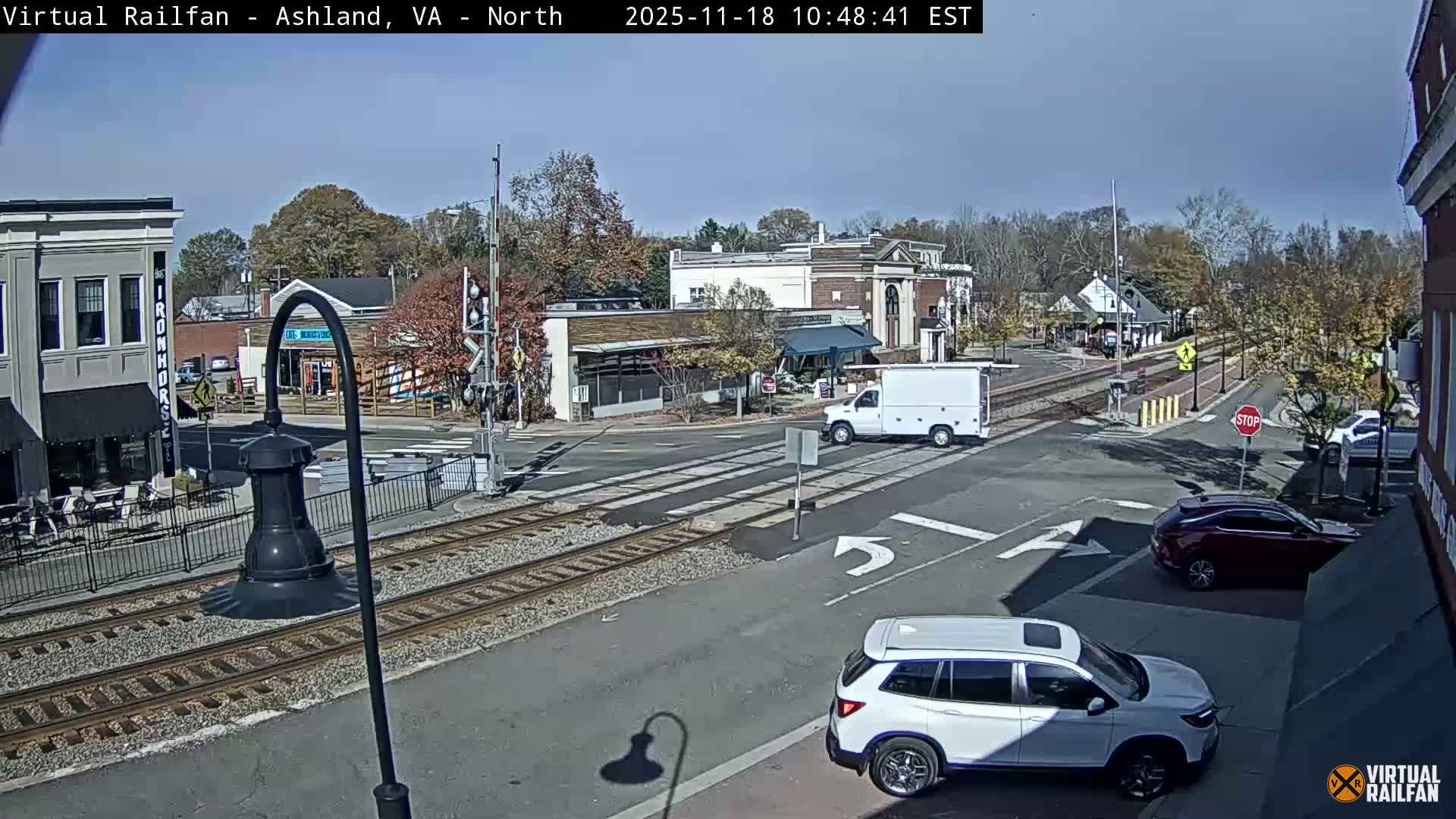 A nighttime street scene shows a quiet intersection with train tracks, streetlights, and several buildings.