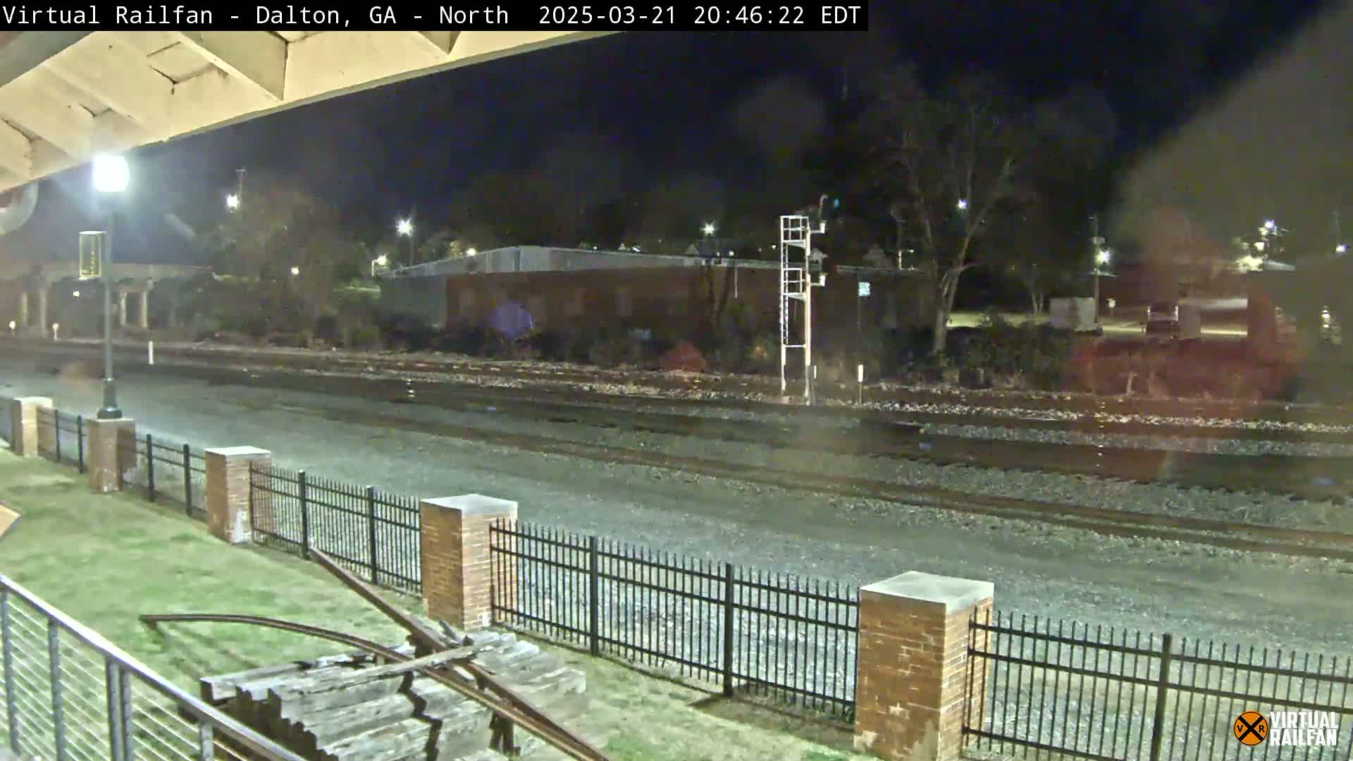 A nighttime view of railroad tracks and a brick fence, under a clear sky.