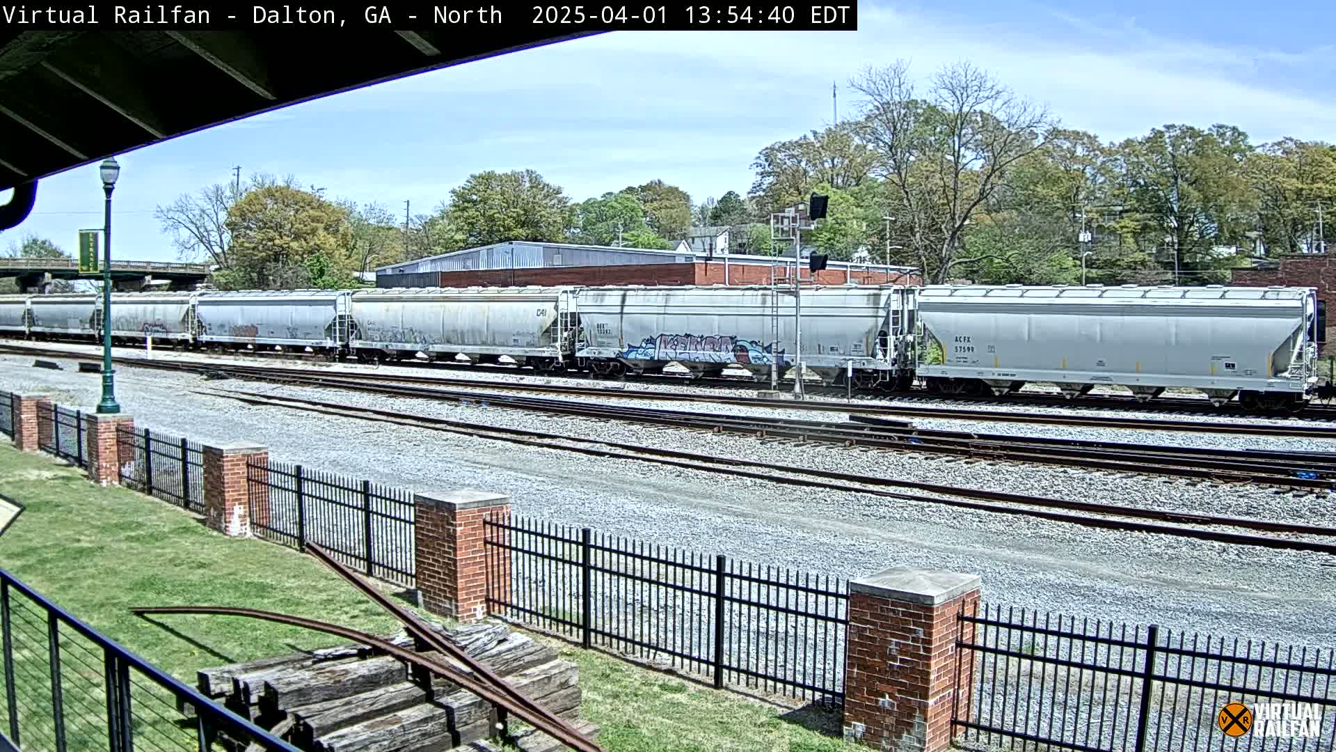 A long freight train of covered hopper cars sits on a rail line under a mostly clear sky.