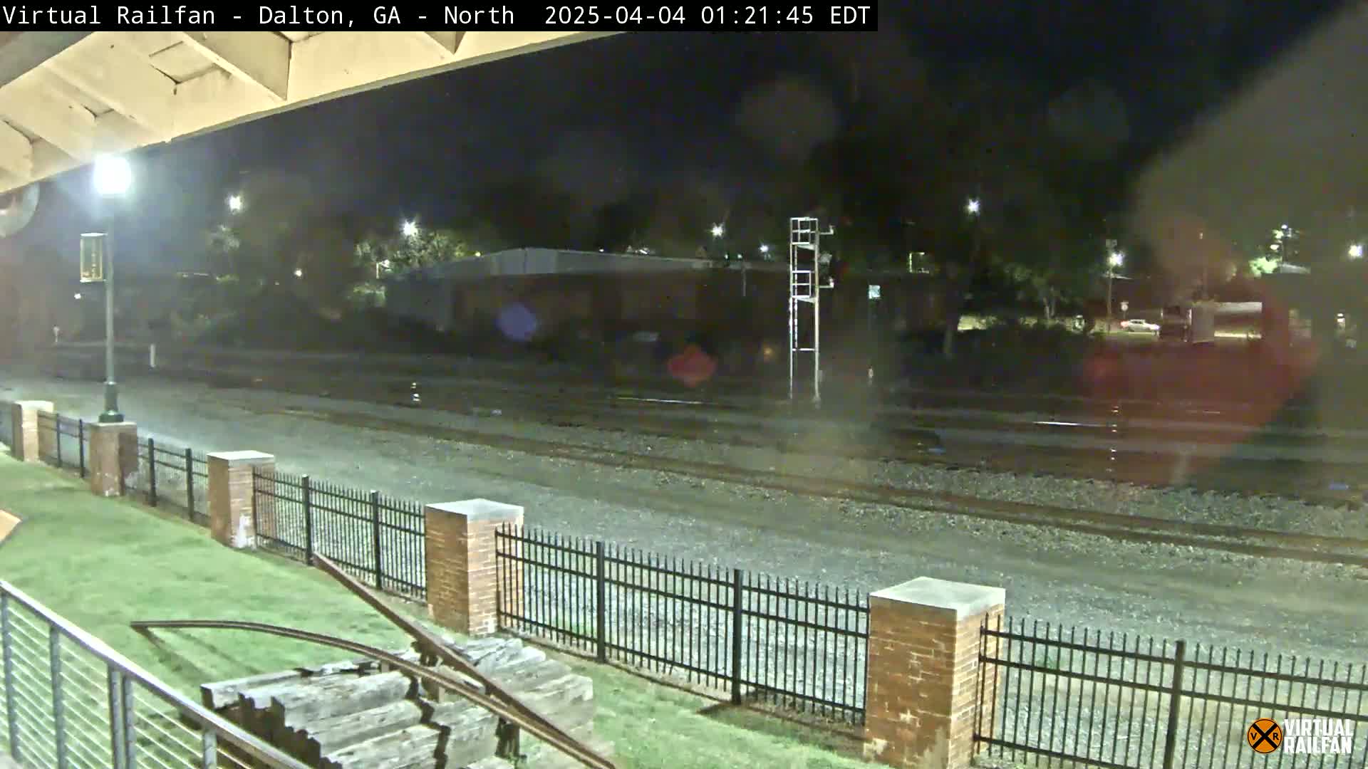 A nighttime view of railroad tracks beside a brick fence, with a few cars visible in the background under a clear sky.