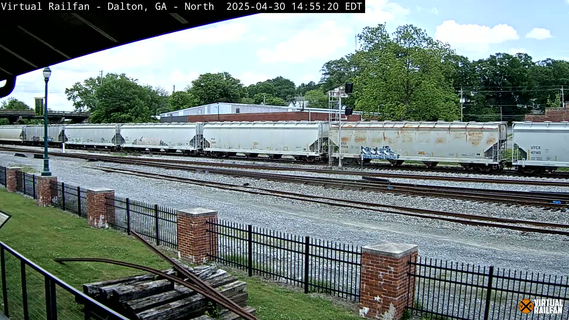 A long freight train of covered hopper cars sits on a rail line under a partly cloudy sky.