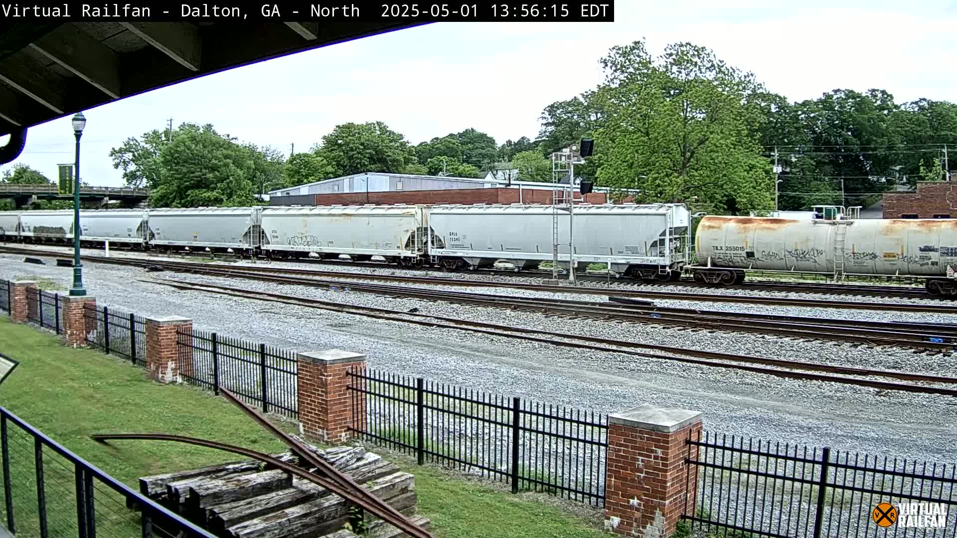 A long freight train of covered hopper cars and a tank car sits on a set of railway tracks under an overcast sky.