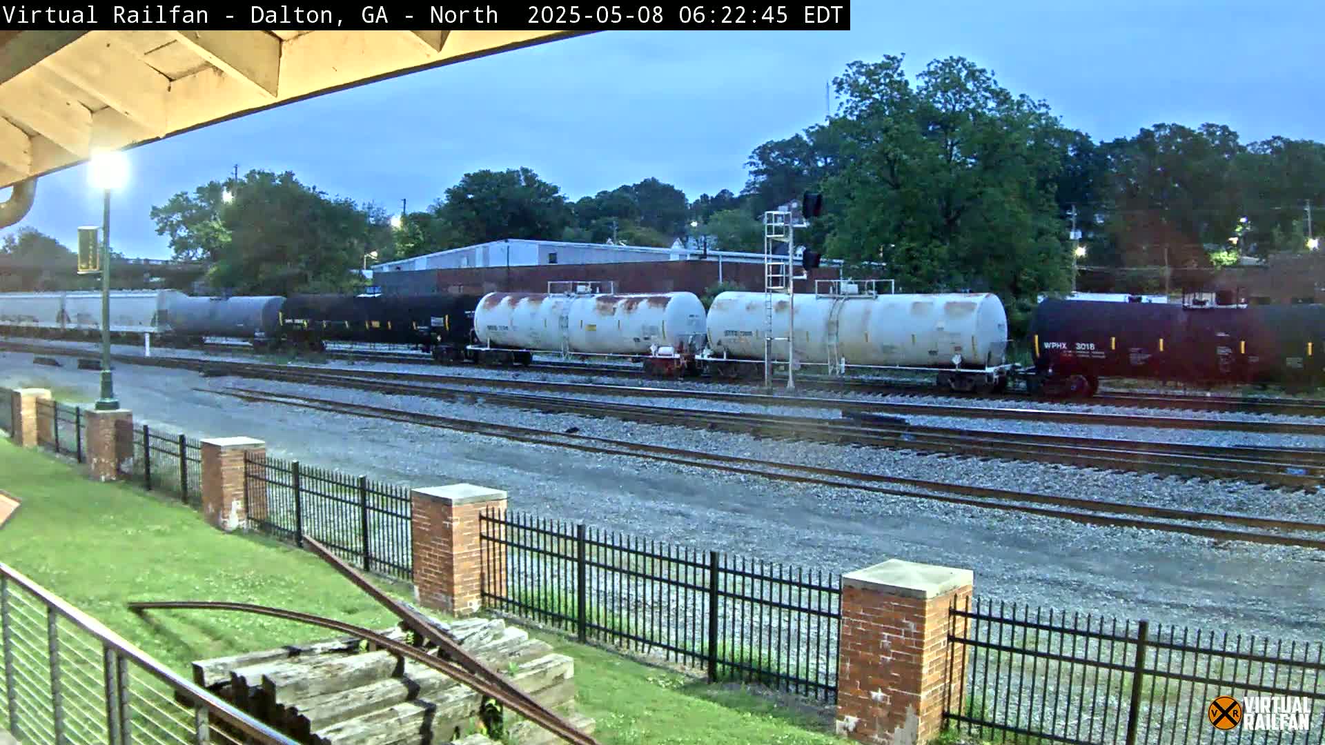 A long freight train of tank cars and boxcars sits on railroad tracks under a twilight sky.