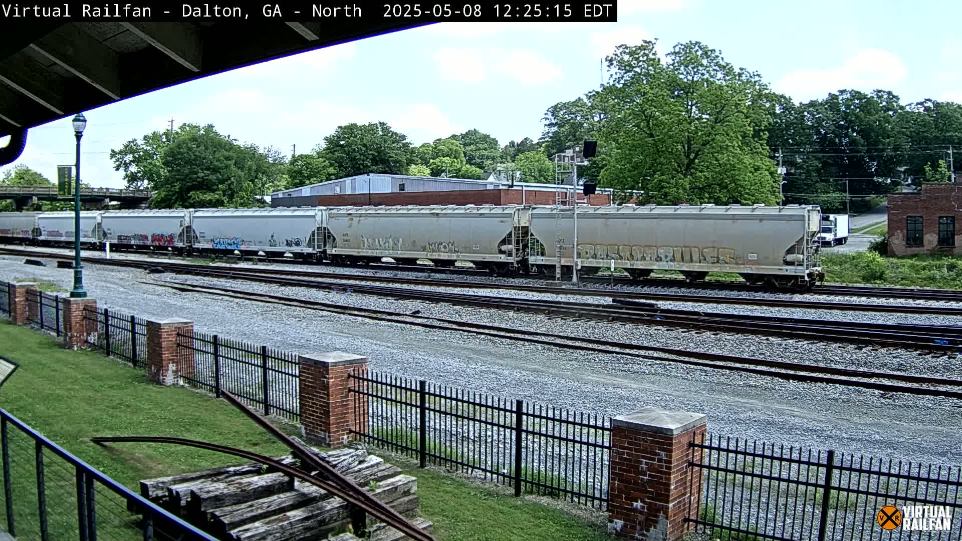 A long freight train with graffiti on its cars sits on a set of train tracks on a partly cloudy day.