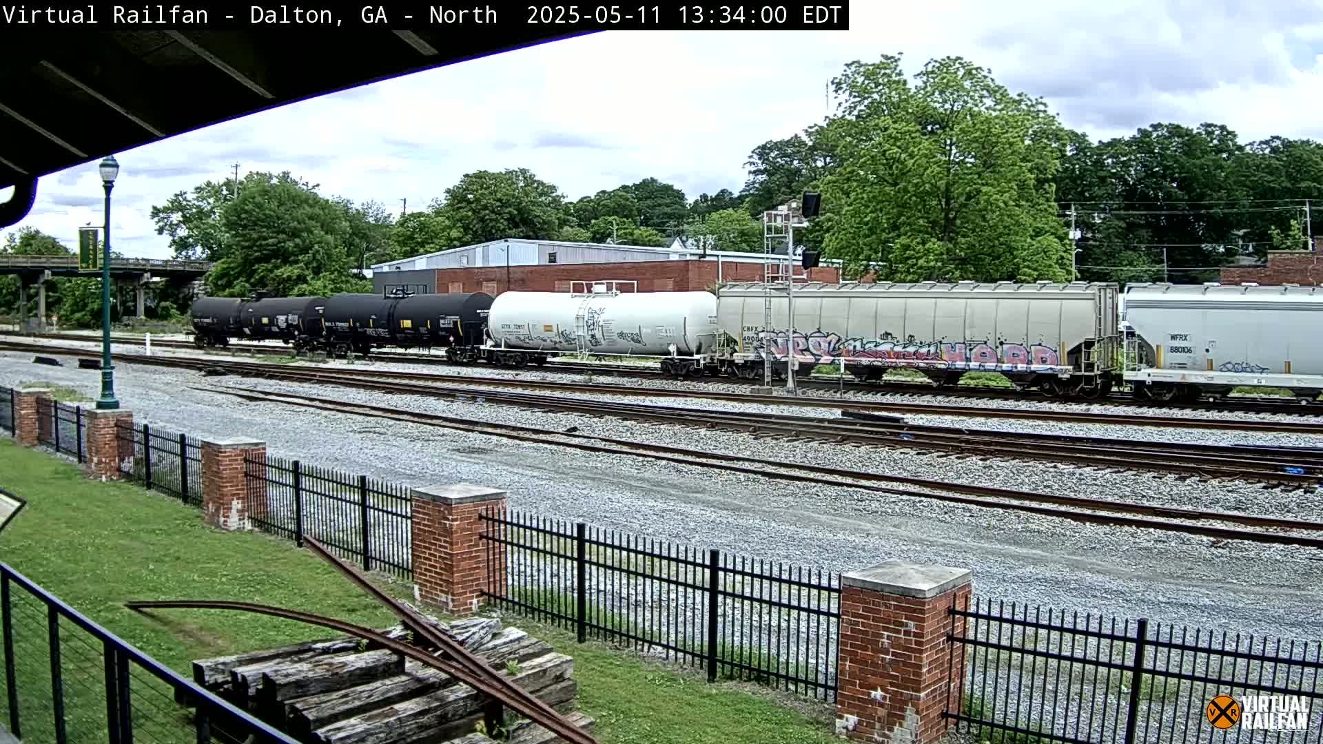 A freight train with several cars, some of which are covered in graffiti, sits on a set of railroad tracks on an overcast day.