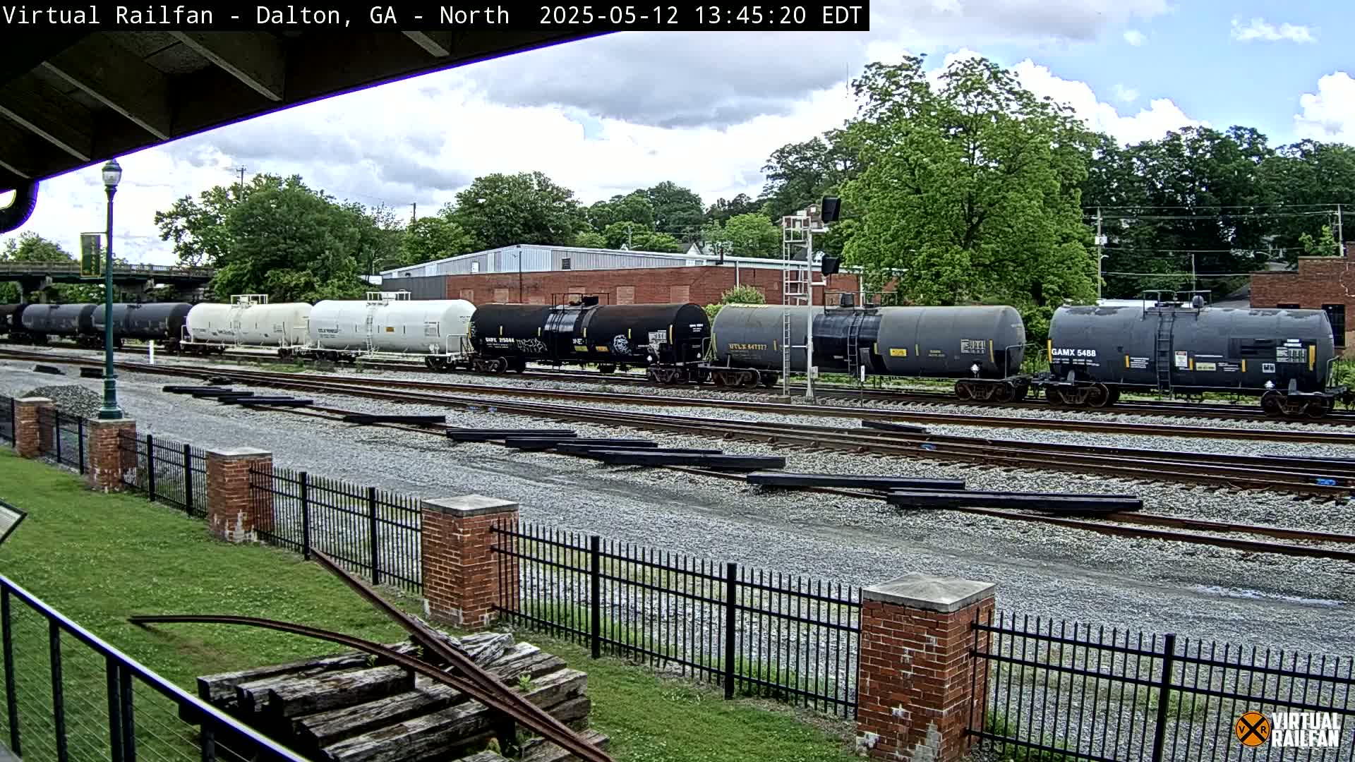 A long line of tanker cars sits on a railway track under a partly cloudy sky.