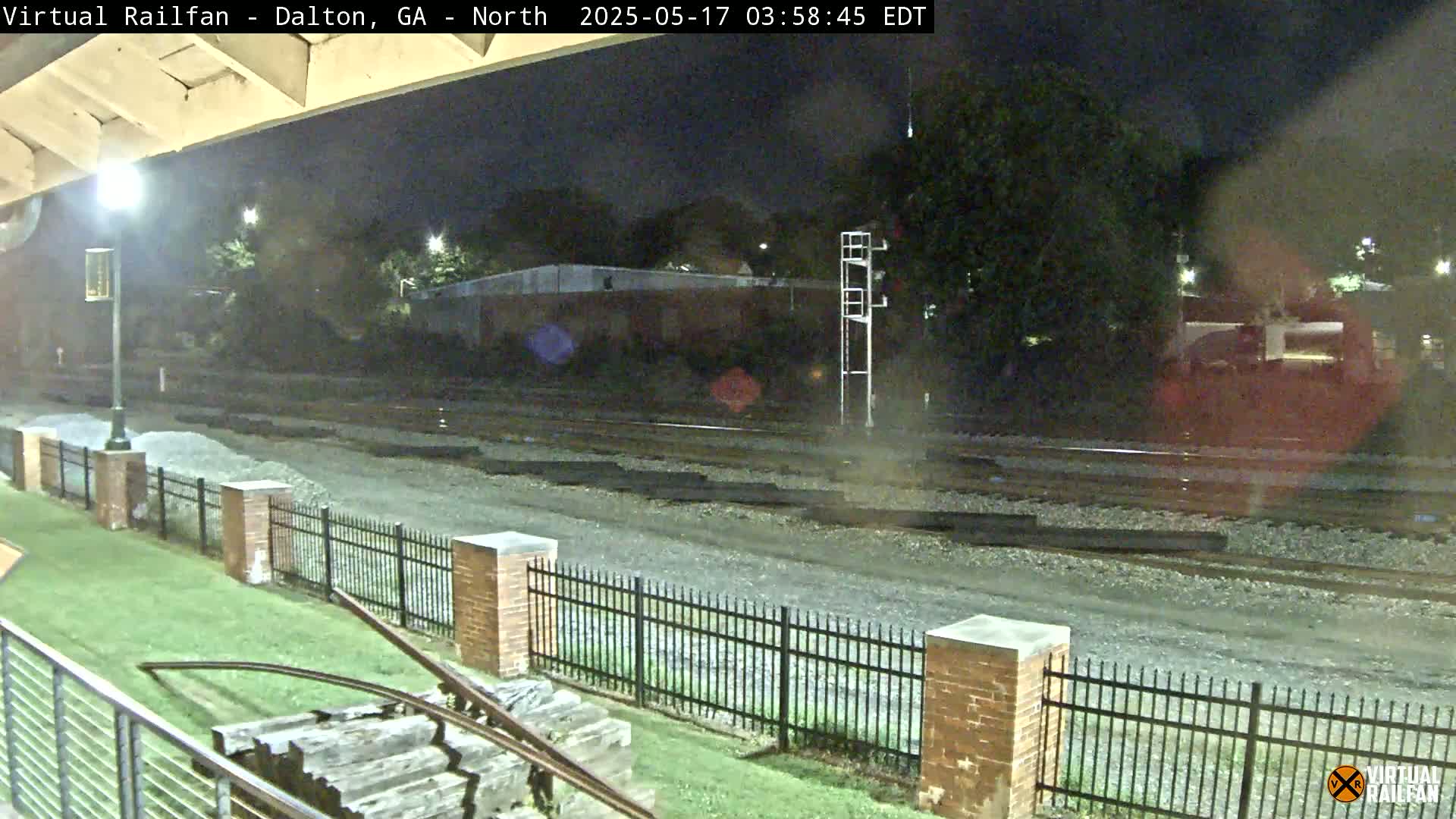 A nighttime view of railroad tracks, a brick fence, and a grassy area, under a clear night sky.