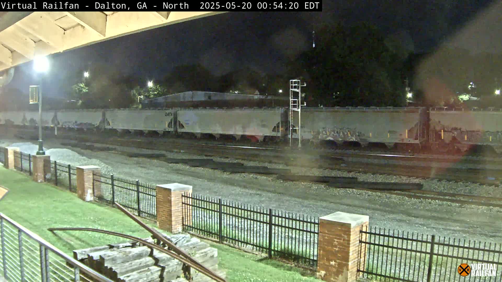 A long freight train sits stationary on railroad tracks at night under a partly cloudy sky.