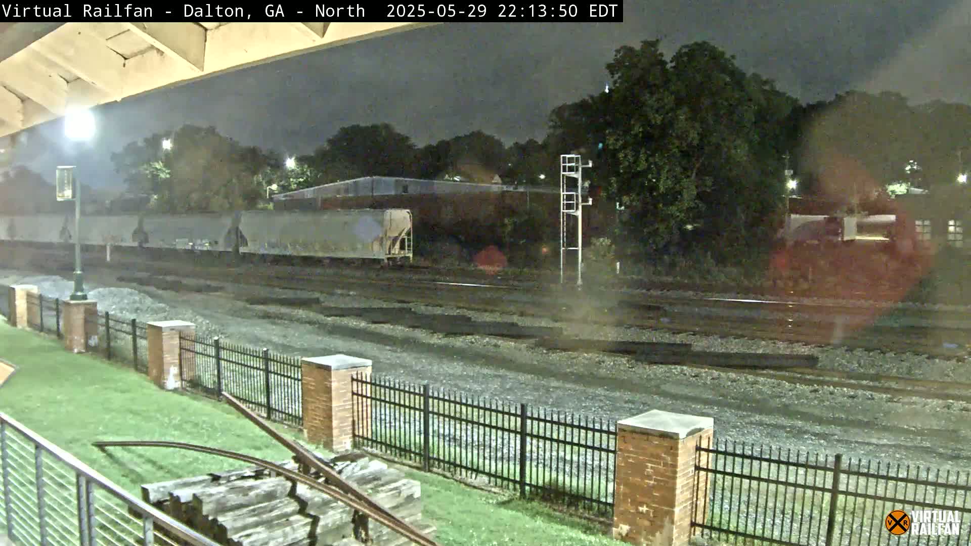 Under a dark night sky, a train sits on railway tracks behind a black metal fence and a grassy area.