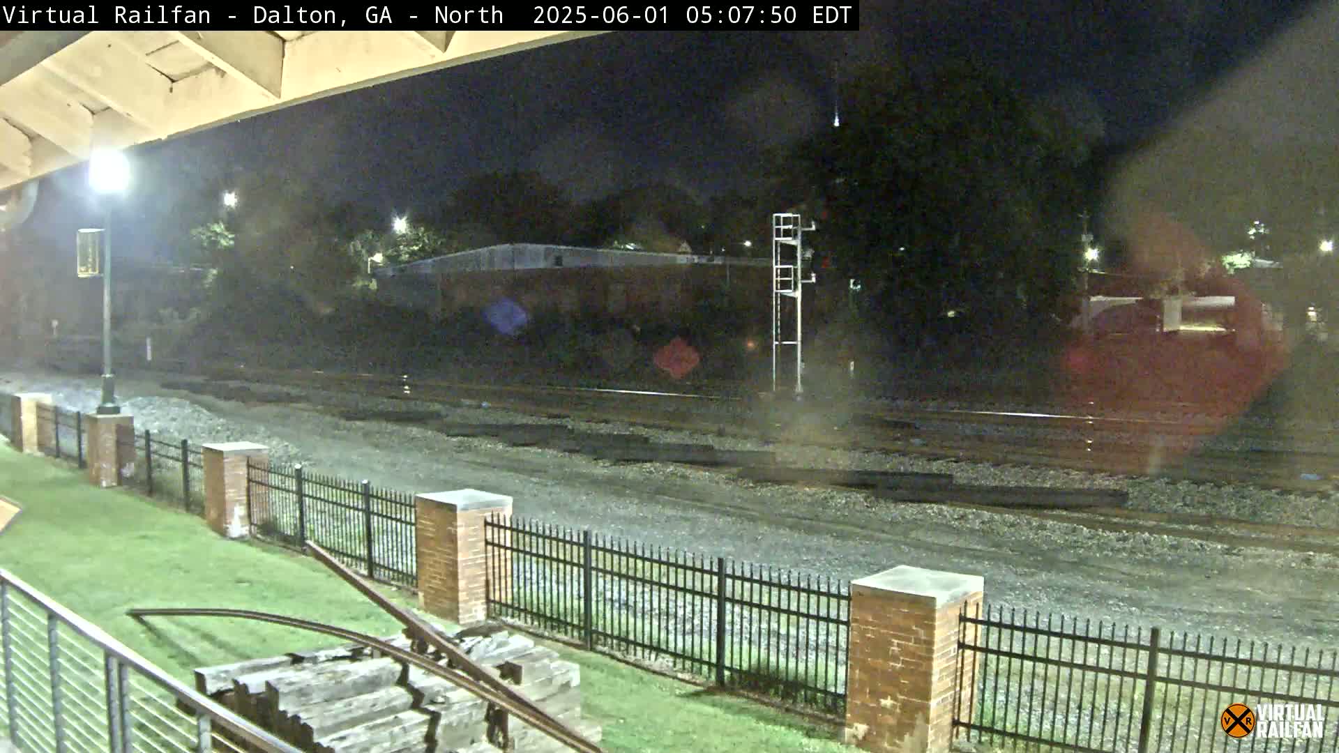 A nighttime view of a railway track, enclosed by a brick fence, with a grassy area visible in the foreground.