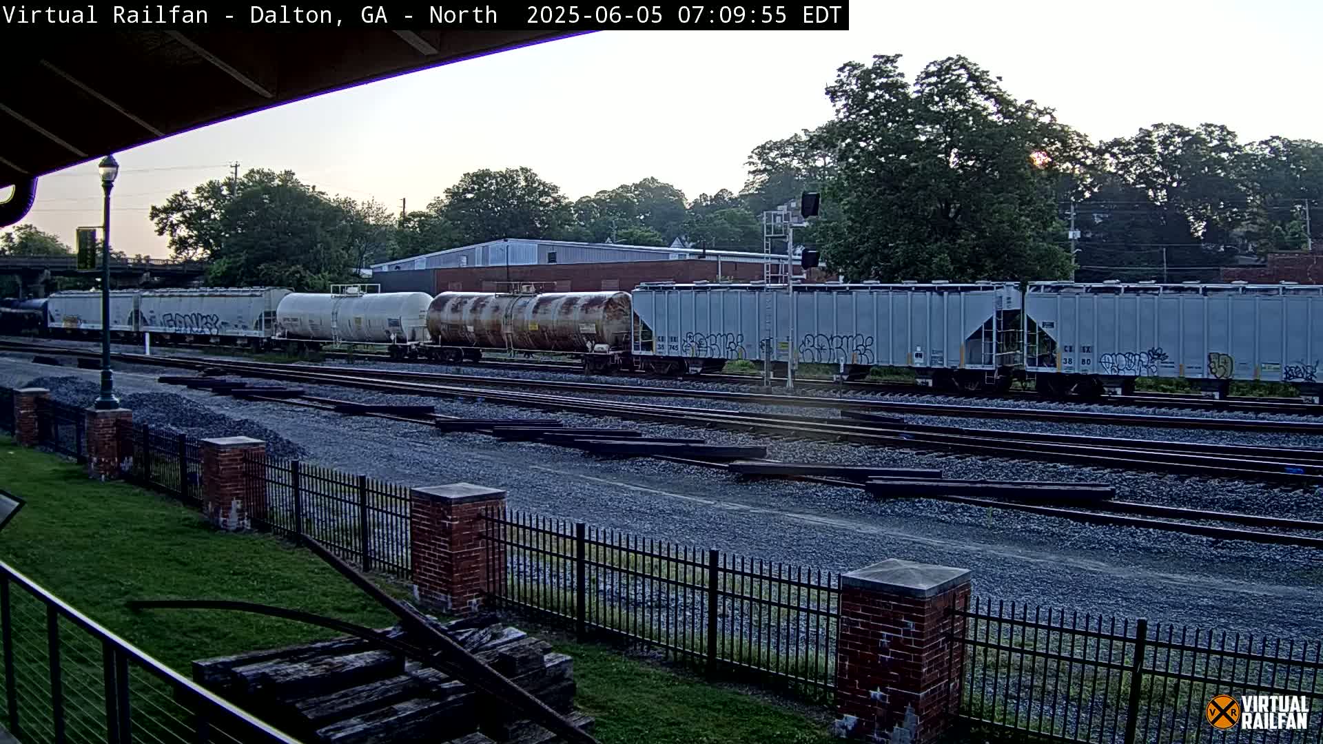 A long freight train sits on a set of railroad tracks under a partly cloudy dawn sky.