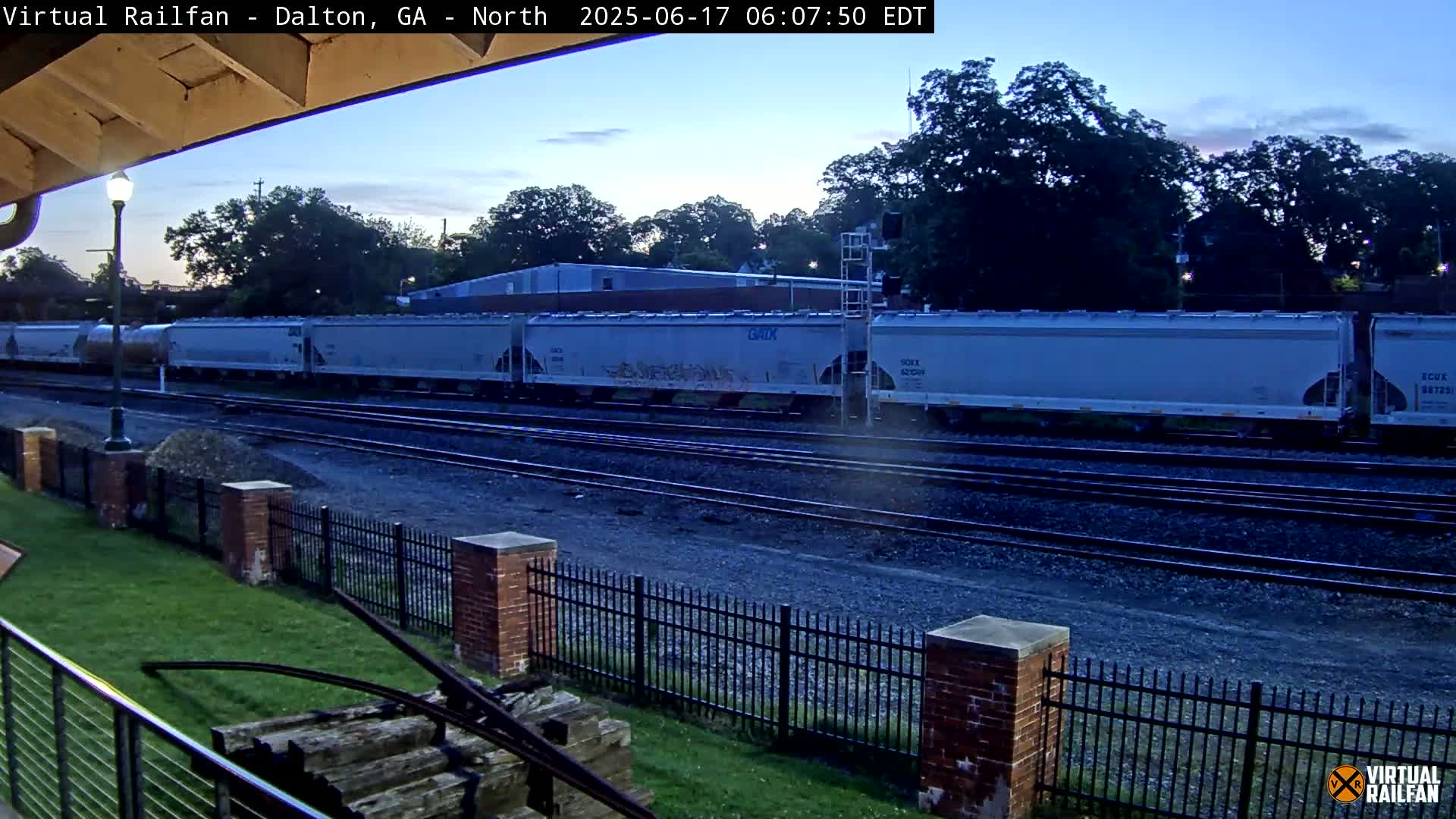 A long freight train of light-grey cars passes by under a twilight sky.
