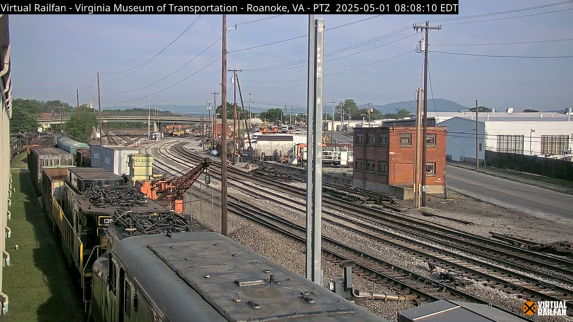A train yard with multiple rail lines, a locomotive, and freight cars under a partly sunny sky.