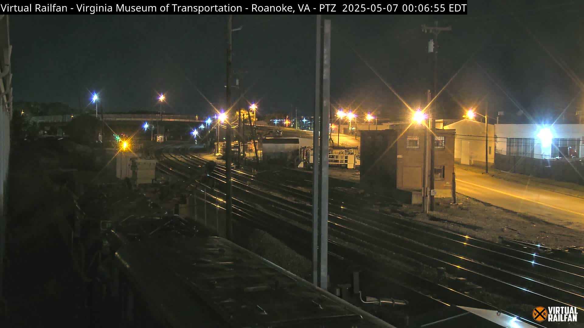 A nighttime view of railroad tracks and industrial buildings, illuminated by streetlights.