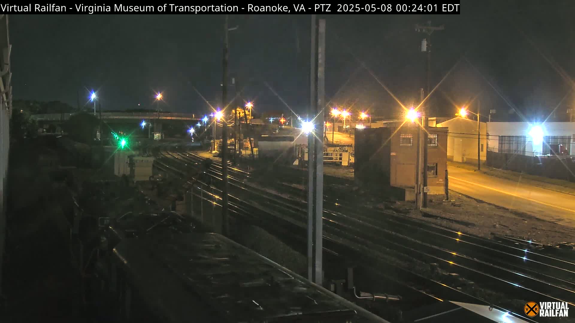 A nighttime view of railroad tracks and industrial buildings under streetlights.