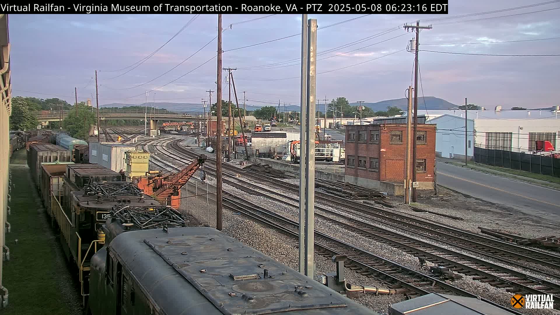 A freight train sits on railroad tracks near a brick building under a partly cloudy, twilight sky.
