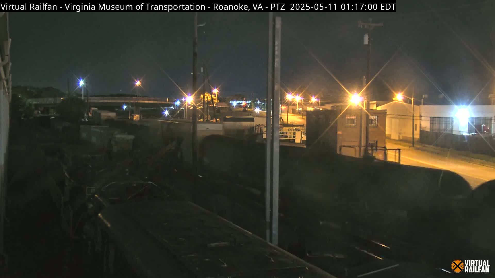 A nighttime view from a train of a dimly lit industrial area with buildings and streetlights.
