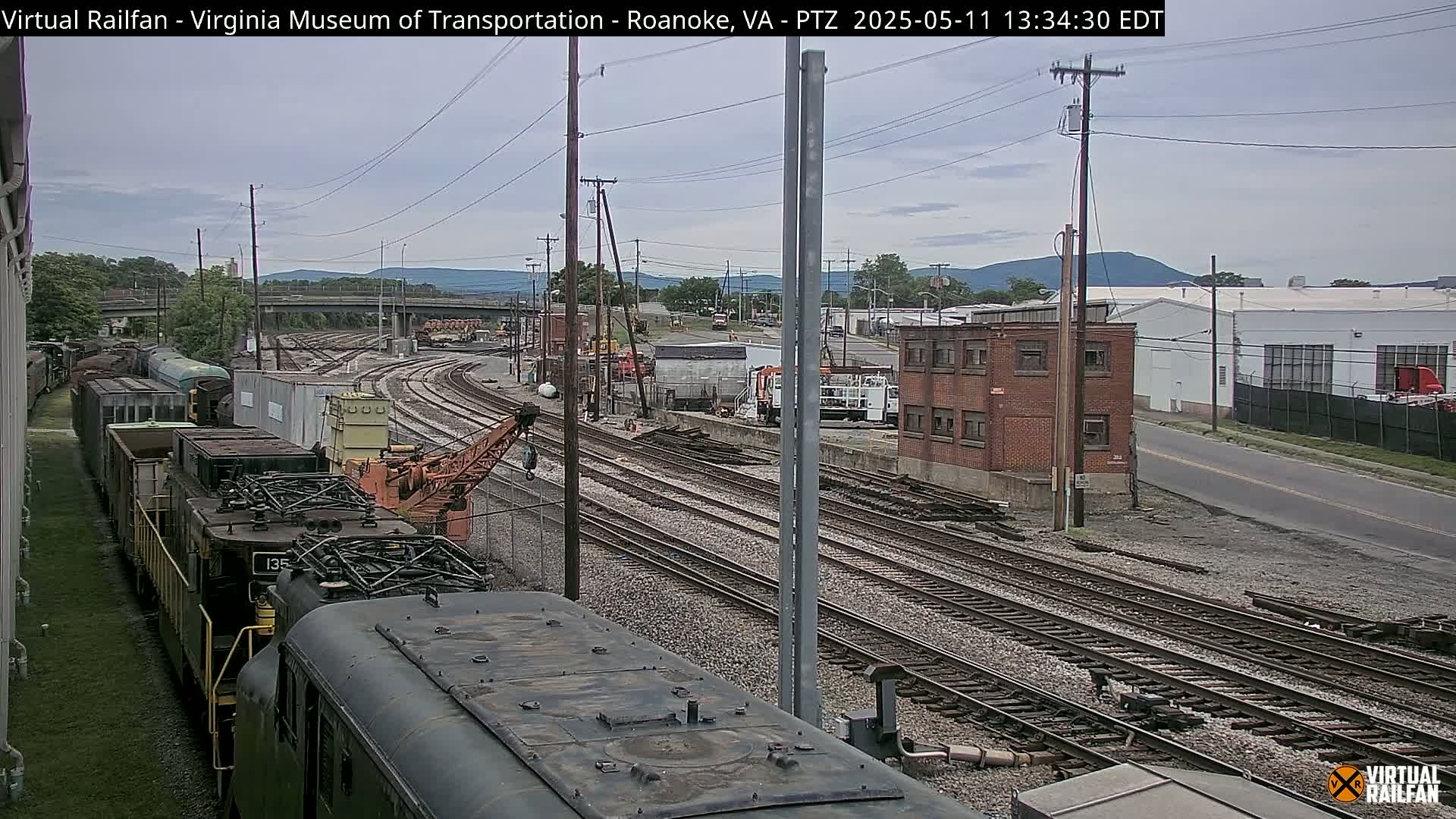 A train yard with multiple sets of railroad tracks under an overcast sky, showing several locomotives and rail cars.