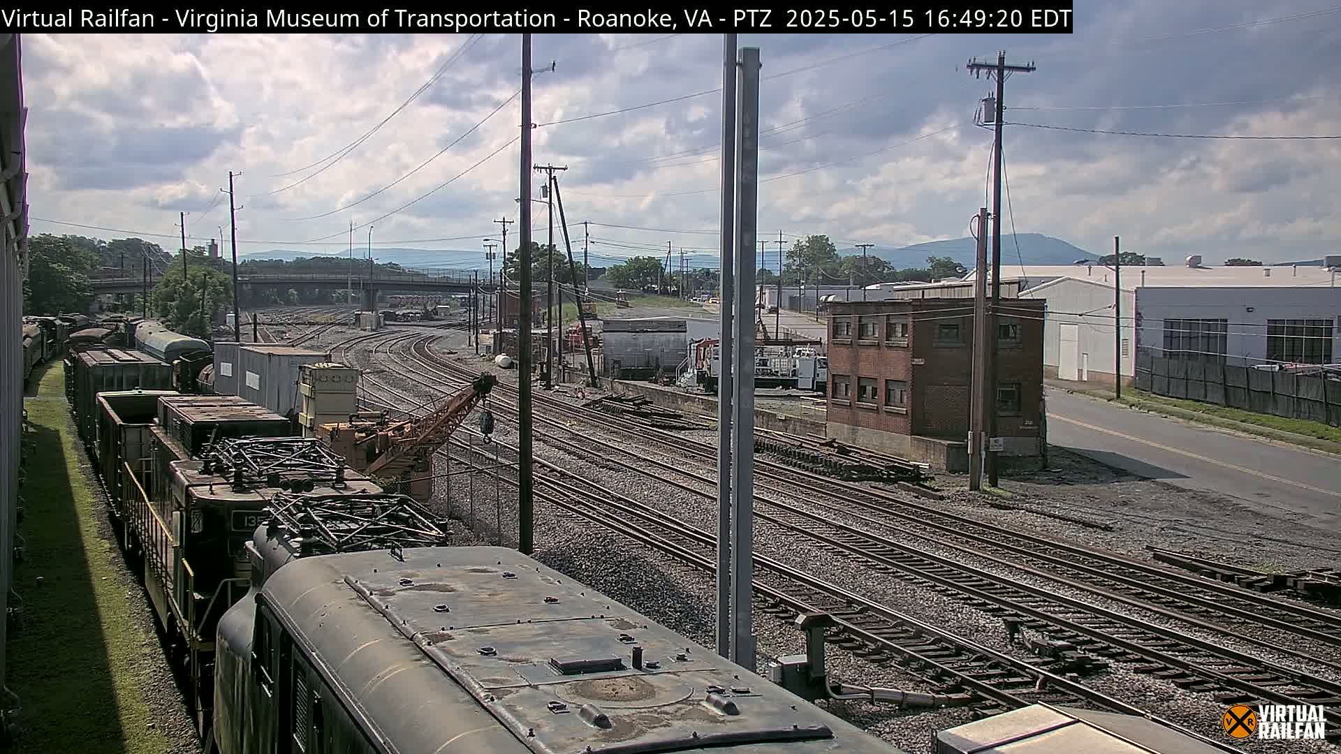 A partly cloudy day reveals a railroad yard with several train cars and multiple tracks, viewed from atop a train car.