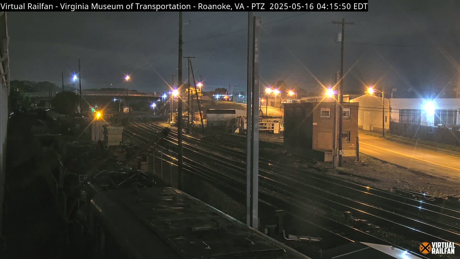 A nighttime view of railroad tracks and industrial buildings under a dark sky.