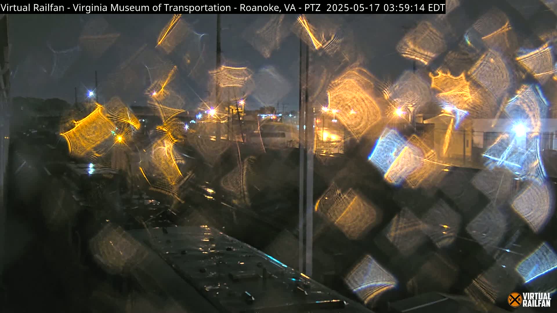 A nighttime view of a rain-streaked window showing blurred lights and buildings beyond.