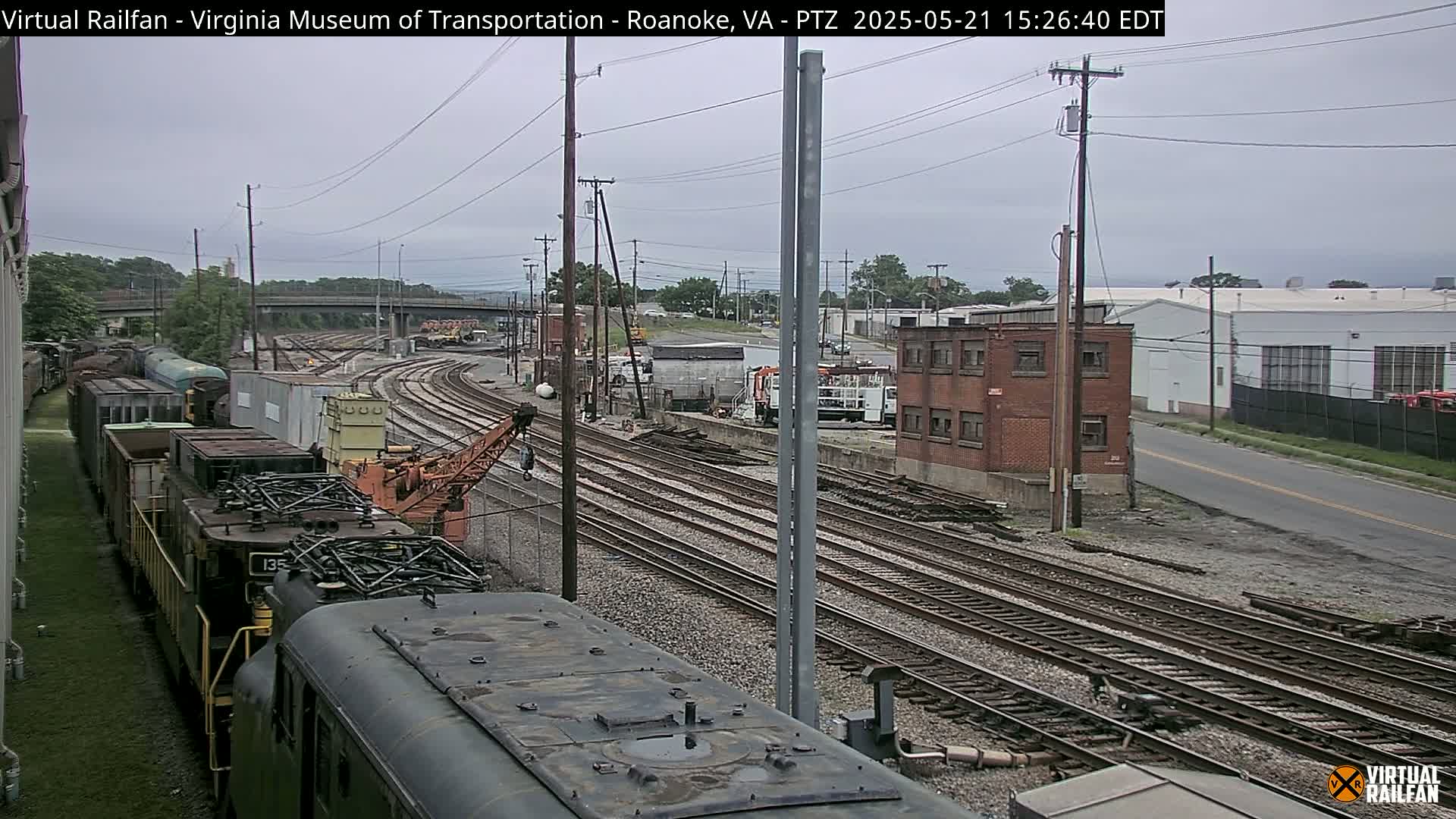 A railroad yard with multiple train tracks, freight cars, and industrial buildings under an overcast sky.