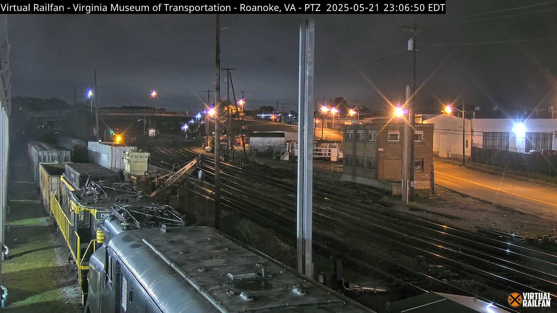 A nighttime view of a railway yard with multiple train cars and tracks, under partly cloudy skies.