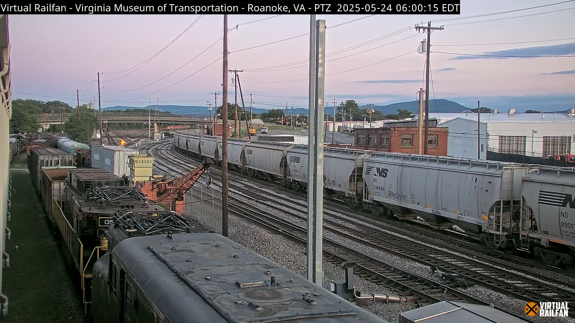 A long freight train, under a twilight sky, sits on a rail yard next to another train.