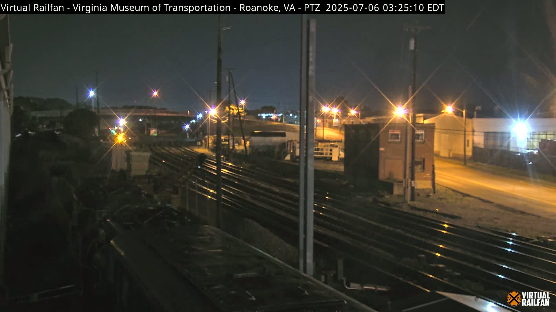 A nighttime view of railroad tracks and industrial buildings, illuminated by streetlights.